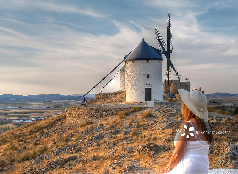 手持玫瑰在日落时分眺望风车的漂亮女人图片素材