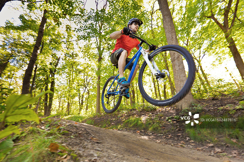 年轻男人在森林小径骑山地自行车图片素材