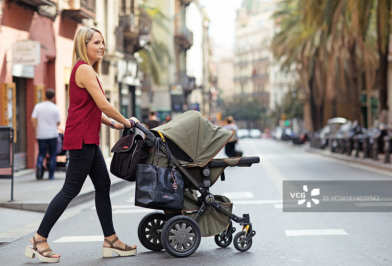 在南欧城市里推着婴儿车的漂亮金发母亲图片素材