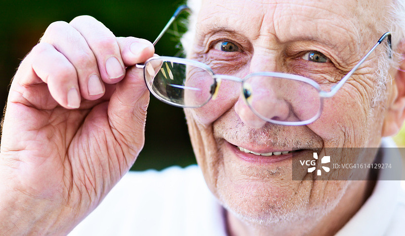微笑的老年男人，视力已矫正，看着他的眼镜图片素材