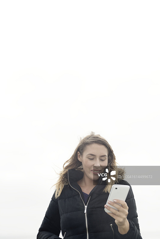 户外看手机的微笑年轻女人图片素材