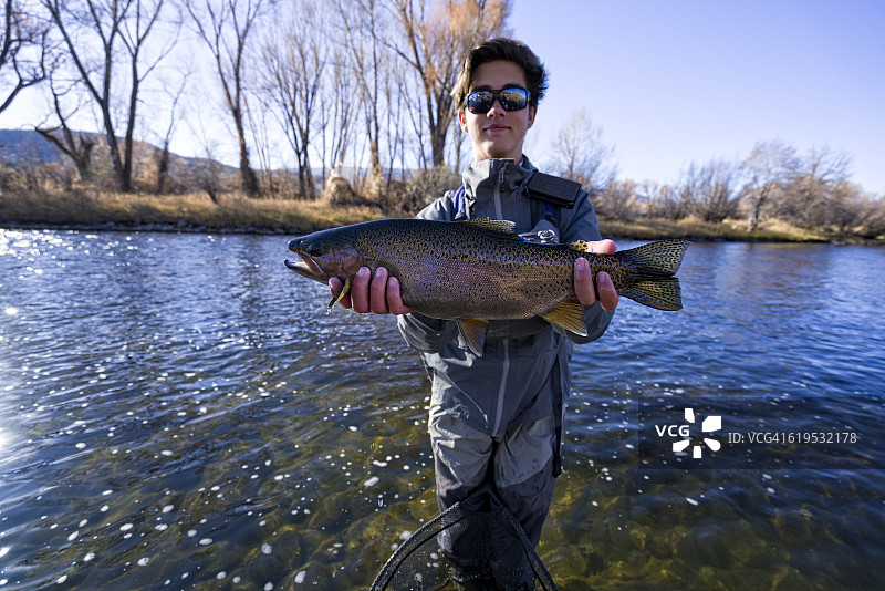 飞蝇钓鱼人手持捕获的虹鳟鱼图片素材