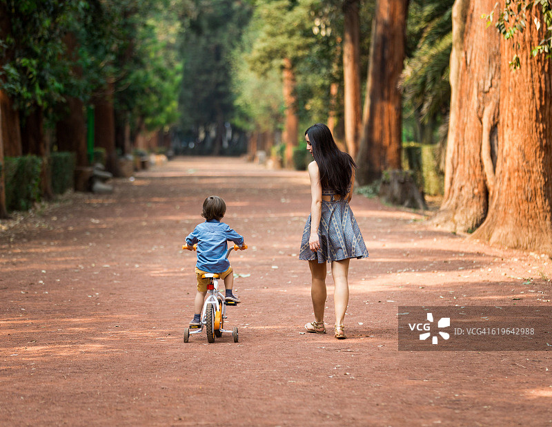 小男孩骑自行车，年轻母亲在旁陪伴图片素材