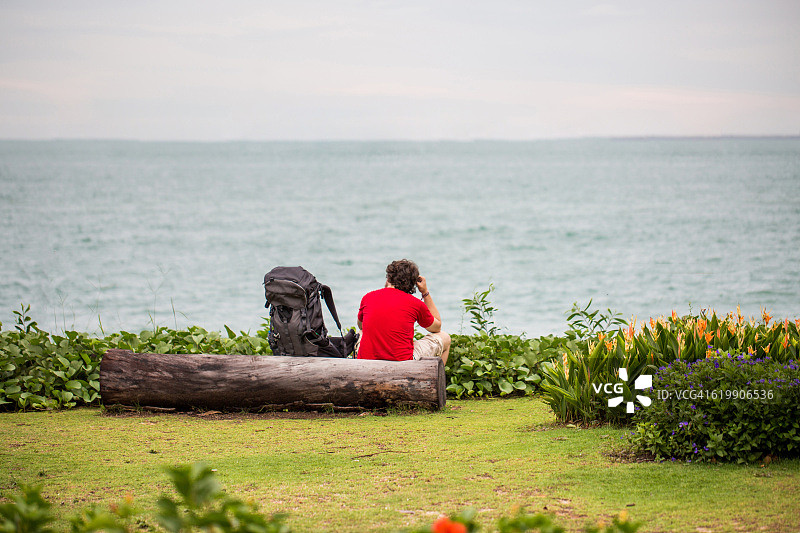 坐在树干上面朝大海的红衣男人图片素材
