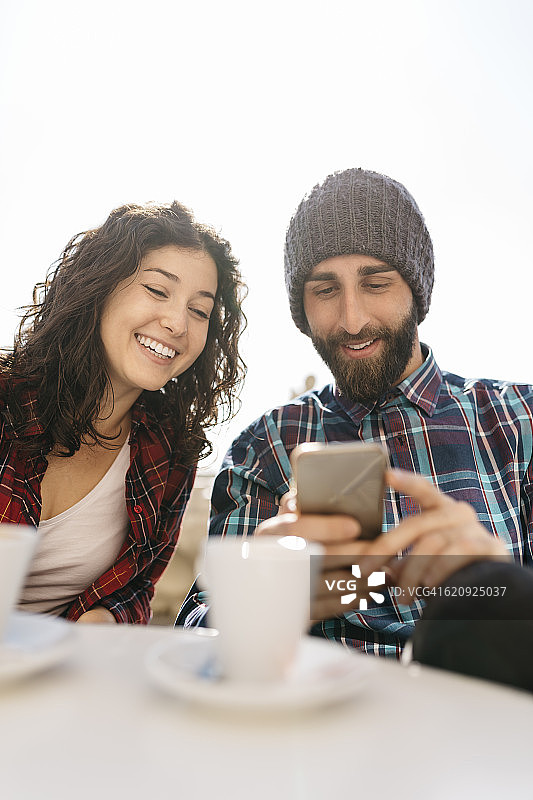 在街边咖啡馆向女友展示手机的年轻男人图片素材