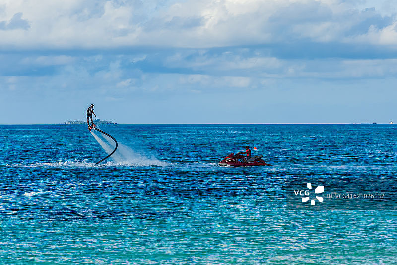 蓝色泻湖中的飞行滑板与水上摩托艇：海上的飞行滑板剪影，专业玩家正在体验名为飞行滑板的全新水上运动，热带夏季水上运动项目图片素材
