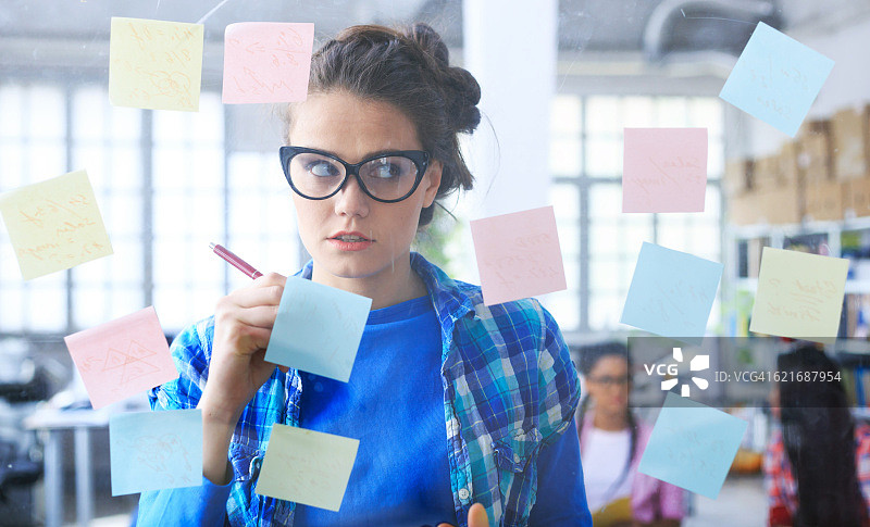 在玻璃墙上写便利贴的女青年图片素材