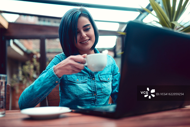 面带微笑的年轻女子在咖啡馆使用笔记本电脑工作图片素材