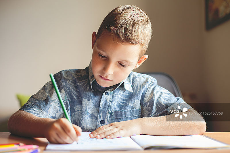 可爱的男孩坐在桌旁做作业图片素材