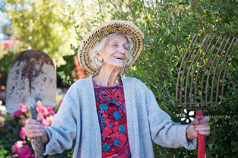 年长的女人在园艺，拿着草叉和耙子，笑着图片素材