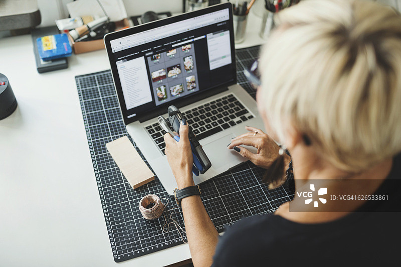 工业设计师在家中办公室使用笔记本电脑并拿着产品的高角度视图图片素材