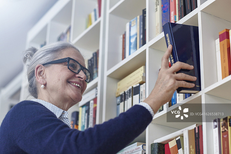 灰发中年妇女从书架上选书图片素材