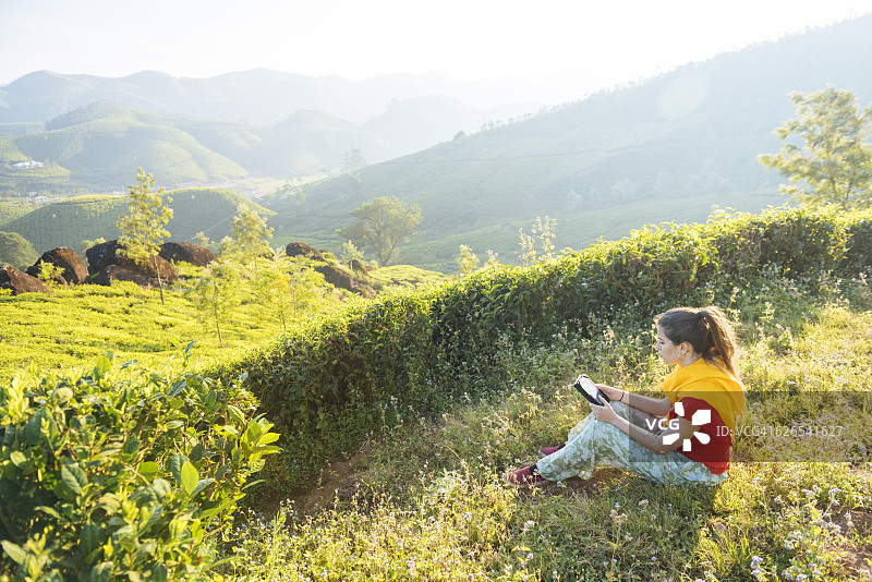 在印度喀拉拉邦蒙纳茶园附近阅读平板电脑的年轻女人图片素材