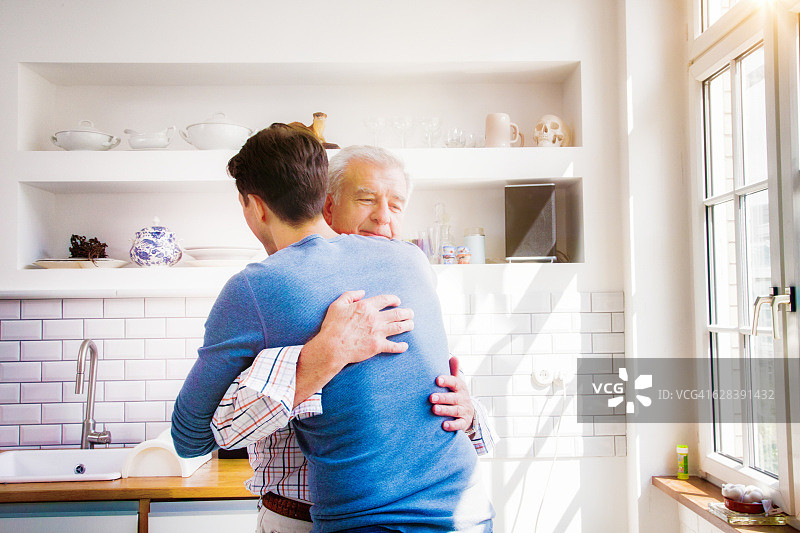 年长的男人在阳光厨房拥抱成年儿子图片素材