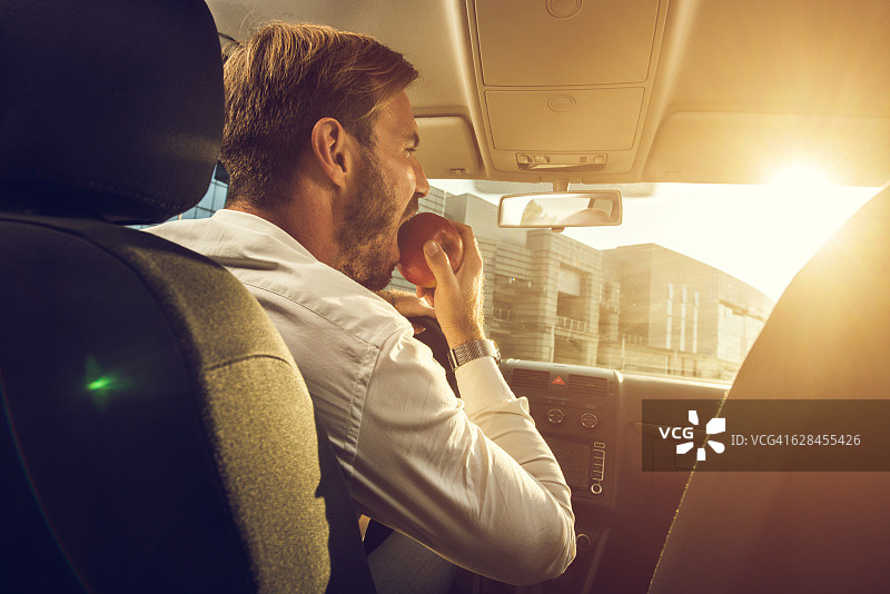 年轻商人在车里吃苹果图片素材