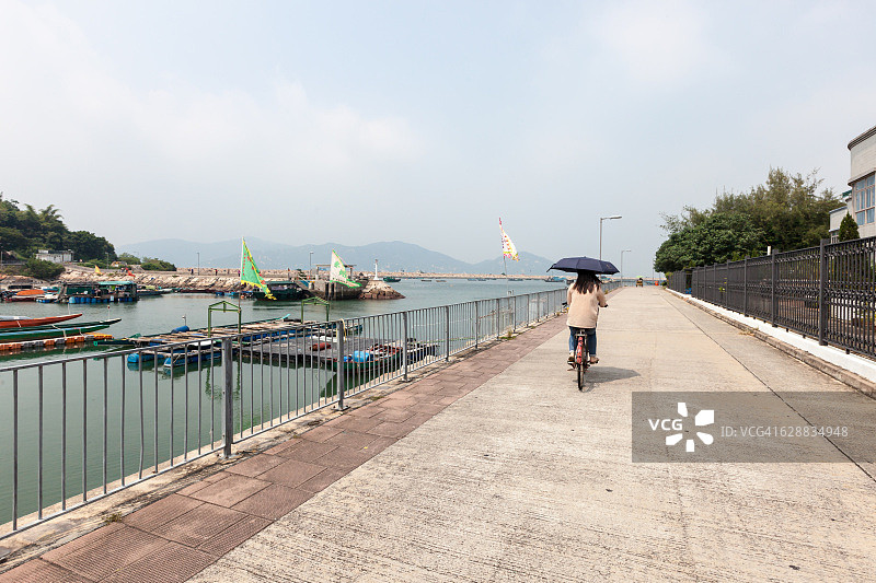 在香港长洲岛的渔港和渔船旁，骑着自行车的撑伞女人图片素材
