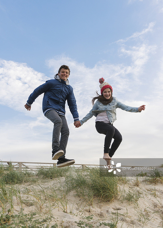 一名年轻男子和一名女子手牵着手在海滩上跳跃图片素材