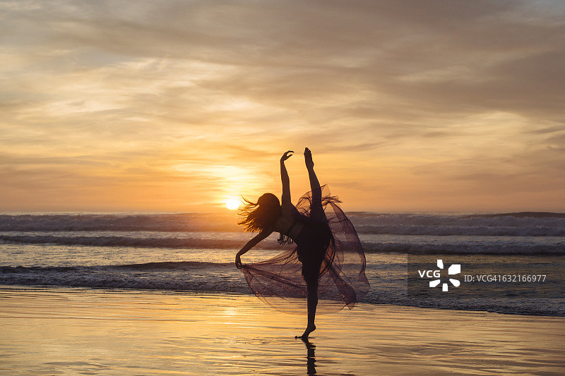 年轻女子在加利福尼亚州圣迭戈海滩夕阳下跳舞图片素材