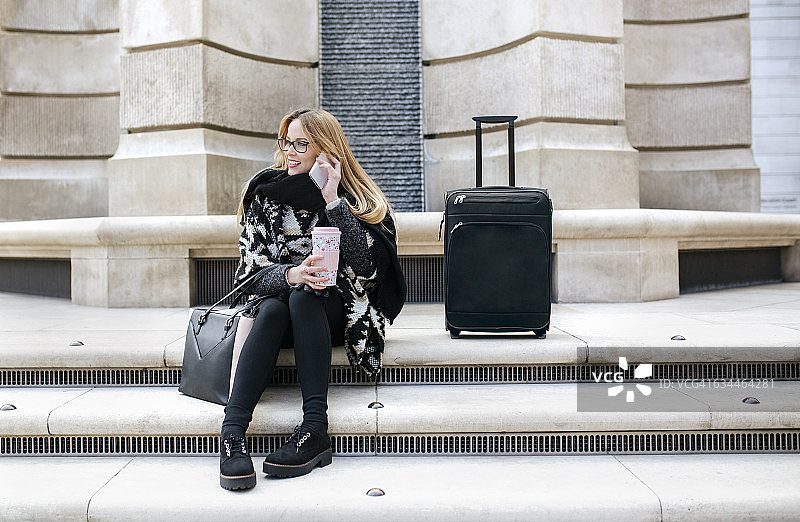 年轻女子在楼梯上用手机，身边有行李图片素材