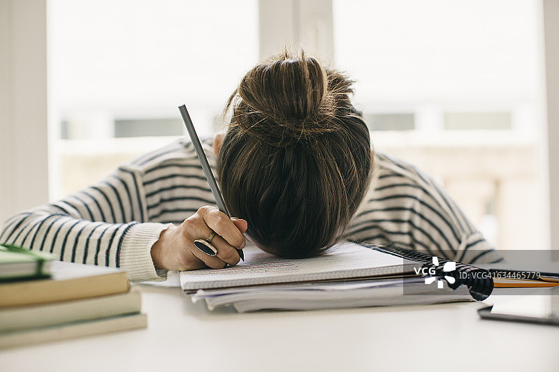 女人在便签本上写字，头靠在桌子上图片素材