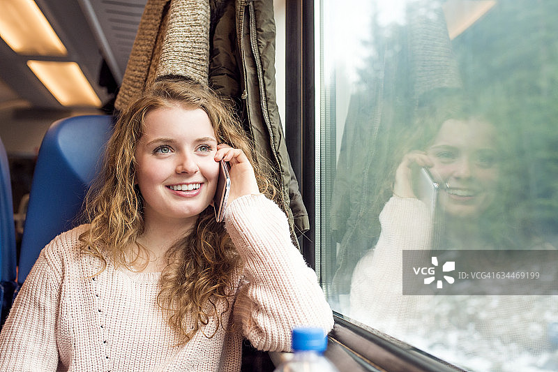 在火车车厢里使用手机的微笑少女图片素材