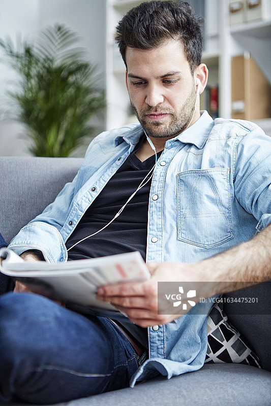 在家戴耳机看杂志的年轻男人图片素材