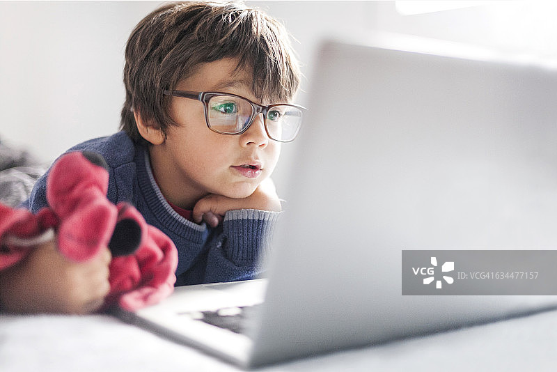 戴着超大眼镜看笔记本电脑的小男孩肖像图片素材