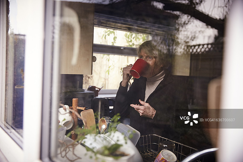 透过窗户拍摄的在厨房喝热饮的年长妇女图片素材