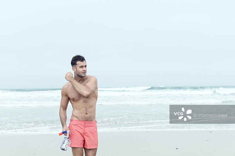 男人穿着泳裤，带着呼吸管在海滩上行走图片素材