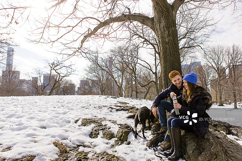 年轻情侣与狗在纽约中央公园雪地里，带着饮料瓶图片素材