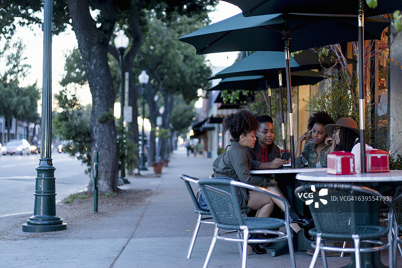一群女性朋友坐在咖啡馆外的桌旁看手机图片素材