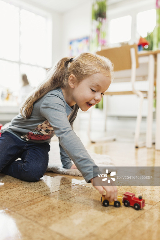 快乐的女孩在教室的地板上玩玩具车图片素材