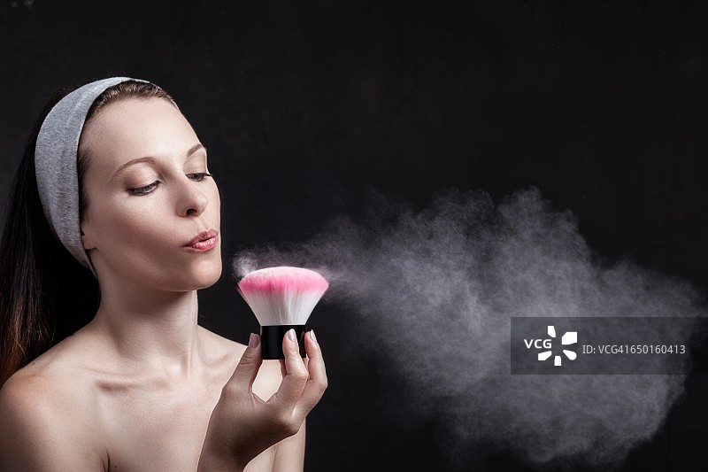年轻女子对着化妆刷吹气图片素材