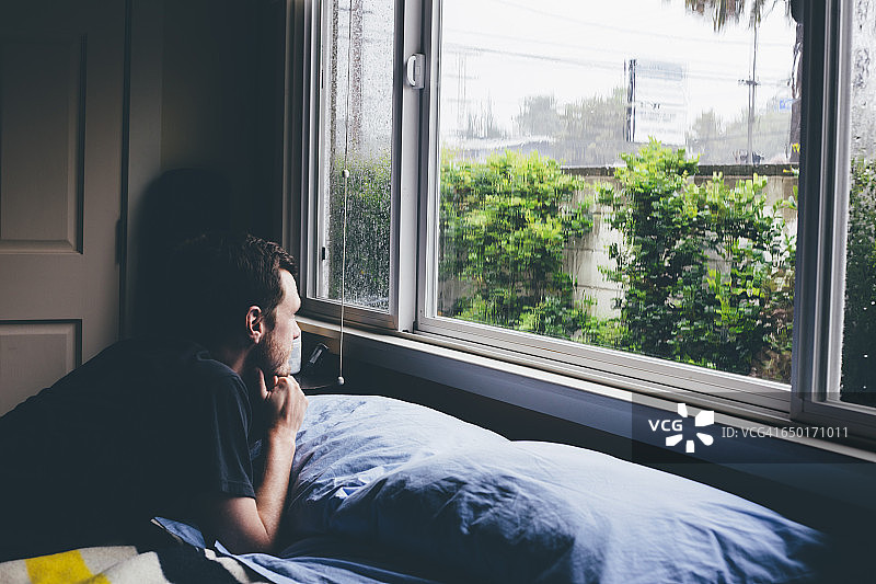 男子躺在床上，望着窗外雨景图片素材