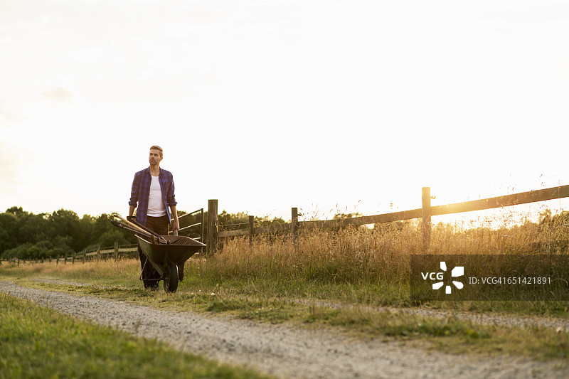 男子在围栏旁的土路上推着独轮车图片素材