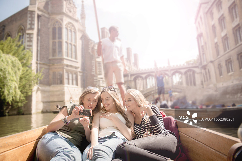 三位年轻女子在剑桥康河上撑篙，看着手机图片素材