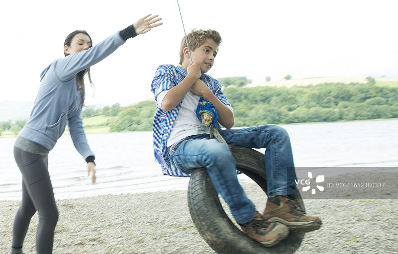 女孩和男孩在威尔士巴拉湖岸边玩挂在树上的轮胎图片素材
