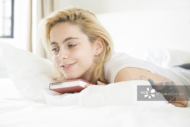 一位有纹身的年轻女子躺在床上看书图片素材