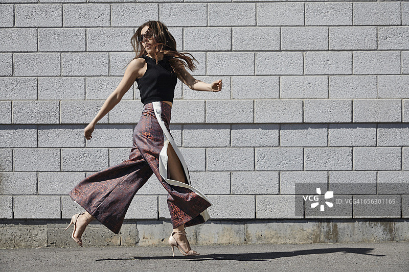 时尚年轻女人经过砖墙图片素材