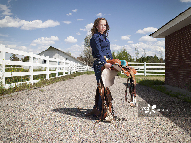 年轻女牛仔在家庭牧场上带着马鞍图片素材