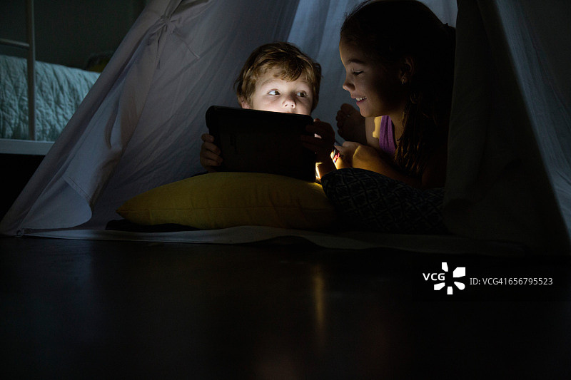 男孩和妹妹在帐篷里使用平板电脑图片素材