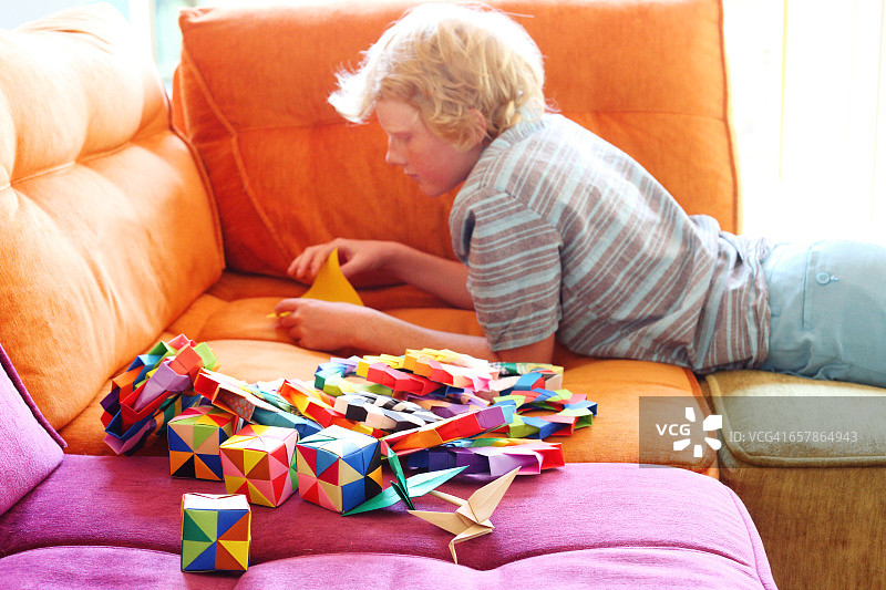 12岁男孩在沙发上制作彩色折纸图片素材