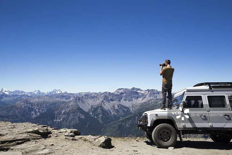 男人站在四驱车顶上远眺群山拍照图片素材