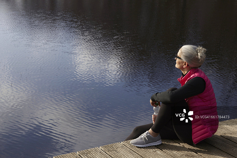 侧面视角：女性坐在木制码头上向远处眺望图片素材