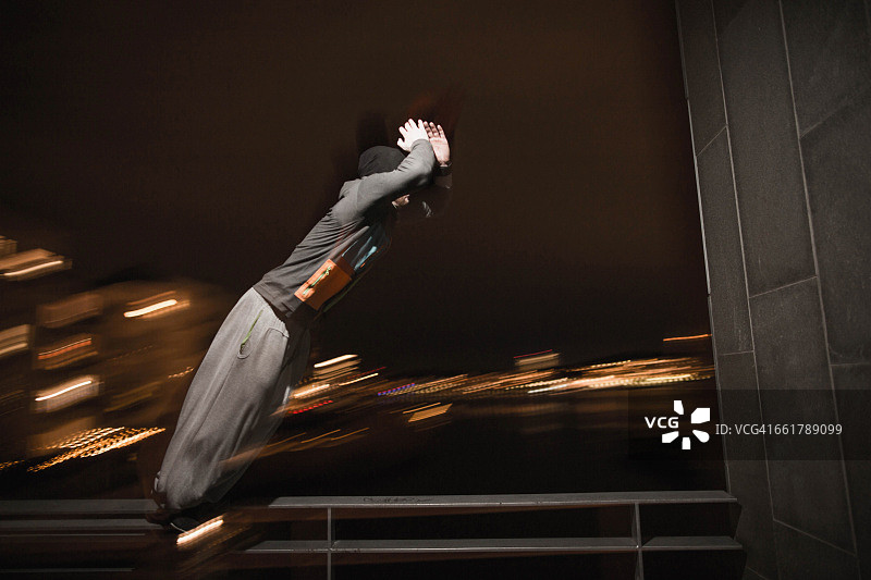 男子在阳台上跳跃的模糊运动，城市灯光背景图片素材