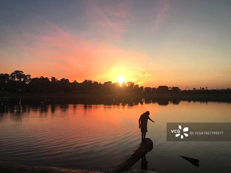 日落时分，加利福尼亚州橙县湖边金属管道上的男孩剪影图片素材