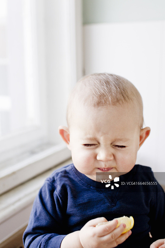品尝柠檬片并做鬼脸的男婴肖像图片素材