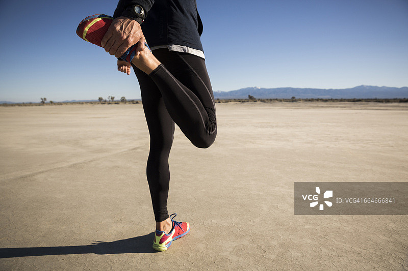 男子在干涸湖床训练拉伸腿部，美国加利福尼亚州埃尔米拉奇图片素材