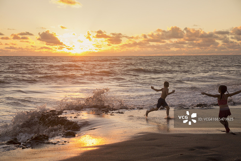日出时分，女孩和哥哥在美国佛罗里达州海滩上奔跑图片素材