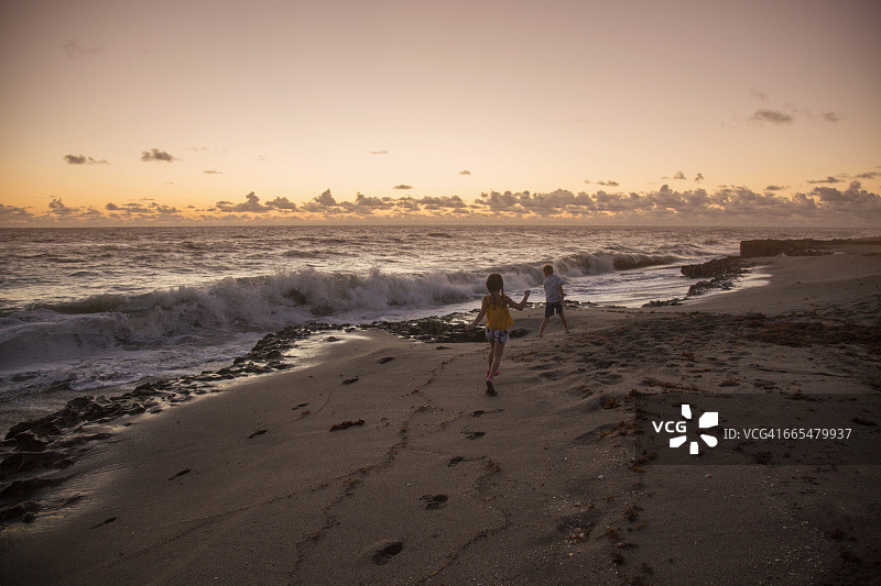 日出时分，男孩和姐姐在海滩上奔跑（美国佛罗里达州朱庇特岛吹岩保护区）图片素材